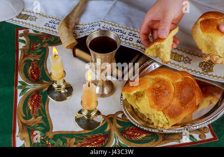 Schabbat-Kerzen im Glas Leuchter i unscharfer Hintergrund überdachte Challah Brot in silbernen Tablett auf weißes Tischtuch. Stockfoto