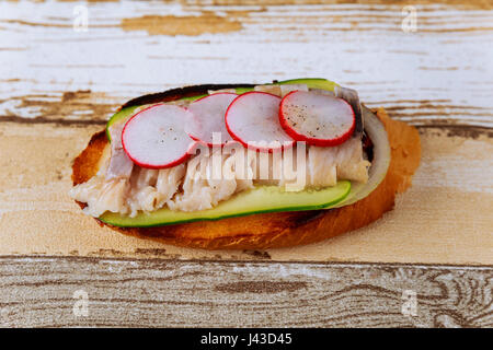 Brötchen mit Hering, saure Gurken, Rettich und Zwiebeln auf Schneidebrett Stockfoto