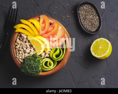 Draufsicht der vegetarische Buddha Schüssel mit grünen Buchweizen, Brokkoli, Avocado, Tomaten und gelbe Paprika Paprika auf dunklen konkrete Hintergrund mit Stockfoto