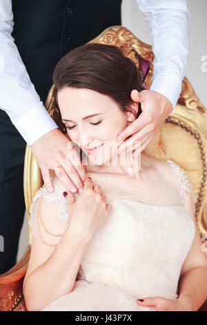 Braut im Kleid und der Bräutigam im schwarzen Anzug auf Sofa im Innenbereich in weisse Studio Interieur wie zu Hause zu sitzen. Trendige Hochzeitsstil. Stockfoto