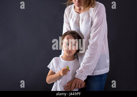 Niedliche kleine Vorschule junge mit großen Beule auf seinem Kopf fallen, umarmt seine Mutter zu Hause und Essen Lutscher Stockfoto