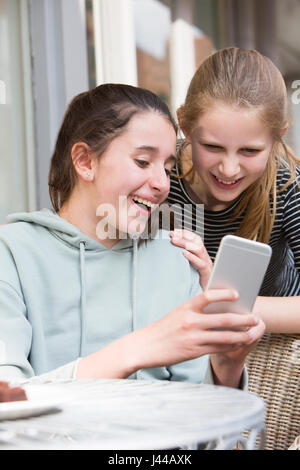 Zwei junge Mädchen im Cafe lesen SMS auf Handy Stockfoto