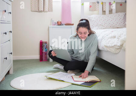 Junges Mädchen am Boden des Schlafzimmers Hausaufgaben auf Laptop Stockfoto