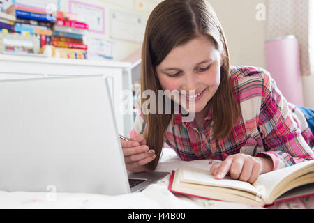 Junges Mädchen auf Bett Hausaufgaben mit Laptop Stockfoto