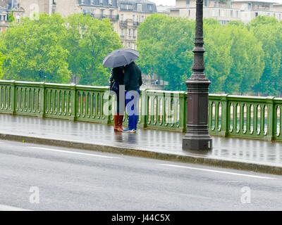 Liebhaber unter einem Sonnenschirm auf einer Brücke über die Seine (Pont de Sully). Küssen in der Regen in Paris, Frankreich. Stockfoto