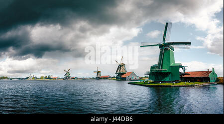 Panoramablick auf authentische Zaandam Mühlen in Zaanstad Dorf am Fluss Zaan gegen den stürmischen Himmel mit Wolken. Wahrzeichen der Niederlande. Stockfoto