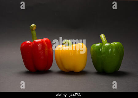 Drei bulgarische Paprika in verschiedenen Farben liegen in einer Reihe auf einem schwarzen Hintergrund. Stockfoto