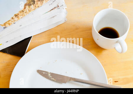 Zeitung, Platte und leere Kaffeetasse links auf einem Tisch nach dem Frühstück Stockfoto