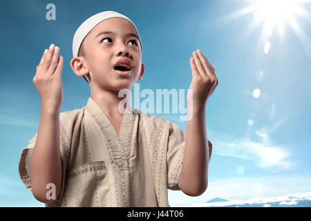 Fröhliches asiatischen muslimische Kind in traditioneller Tracht mit blauem Himmelshintergrund beten Stockfoto