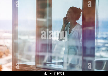 Lächelnde Reife Geschäftsfrau in Bürogebäude und reden über Handy. Weibliche executive tatenlos Glasfenster mit Handy. Stockfoto