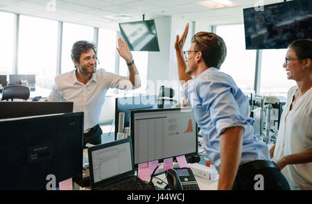 Erfolgreiche Geschäftsleute suchen glücklich und geben hohe fünf. Kolleginnen und Kollegen feiern Erfolg im Büro. Stockfoto