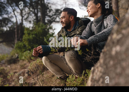 Paar eine Pause nach dem Wandern bergauf auf dem Lande. Junger Mann und Frau sitzen auf Berg und wegsehen.