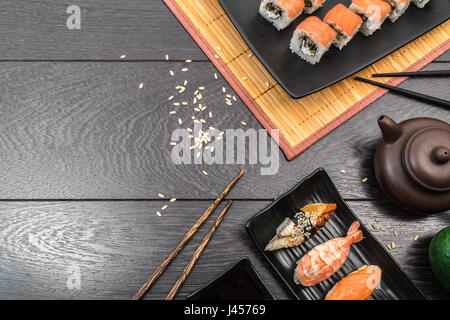 Sushi set Sushi, Sashimi, Nigiri und Maguro Brötchen auf Platte und Teekanne auf dunklem Holz serviert. Platz für Text. Stockfoto