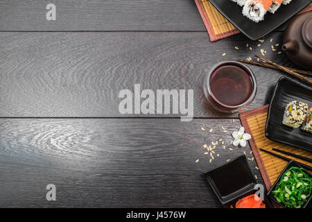Sushi einstellen-Sashimi und Sushi Rollen auf Platte serviert mit Teekanne und Teabowl und weiße Blumen auf dunklem Holz Hintergrund Platz für Text. Stockfoto