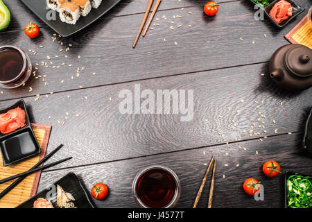 Sushi set Sushi, Sashimi, Nigiri und Maguro Brötchen serviert auf Platte mit Teekanne und Tomaten auf dunklem Holz. Platz für Text. Stockfoto
