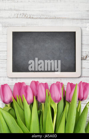 Rosa Tulpen mit Tafel über schäbigen weißen hölzernen Hintergrund, Ansicht von oben Stockfoto