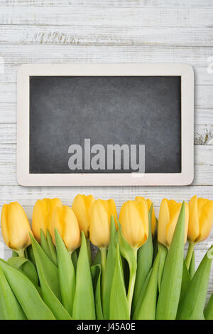 Gelbe Tulpen mit Tafel über schäbigen weißen hölzernen Hintergrund, Ansicht von oben Stockfoto