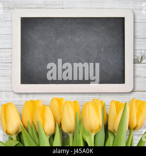 Gelbe Tulpen mit Tafel über schäbigen weißen hölzernen Hintergrund, Ansicht von oben Stockfoto