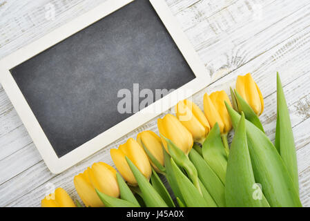 Gelbe Tulpen mit Tafel über schäbigen weißen hölzernen Hintergrund, Ansicht von oben Stockfoto