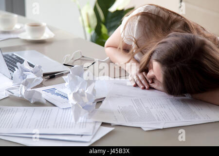 Frau schläft auf Schreibtisch bedeckt zerknitterten Papiere Stockfoto