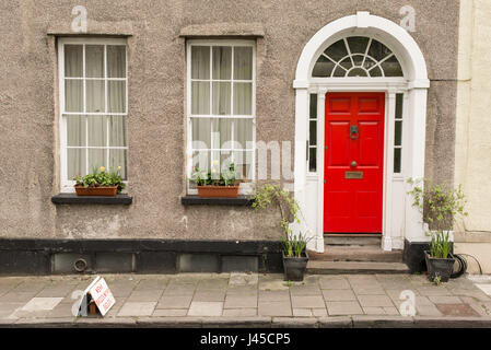 Fassade des britischen Traditionshauses mit grauen Wänden, rote Tür und zwei Fenster mit Blumen auf dem Balkon Stockfoto