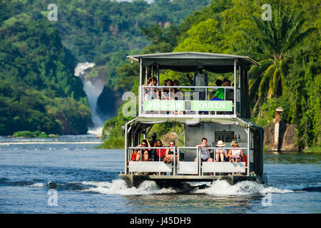 Tour Boot mit Touristen auf Victoria Nil mit Murchison Falls im Hintergrund, Uganda Stockfoto