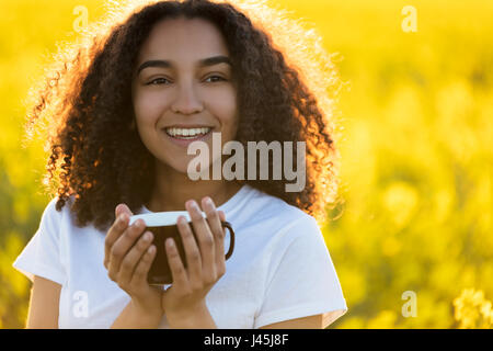 Schöne glückliche Mischlinge afroamerikanische Mädchen Teenager weibliche junge Frau lächelt trinken Kaffee oder Tee im freien Stockfoto