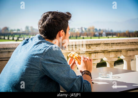 Junger Mann Betrieb Sandwich beim Sitzen im café Stockfoto
