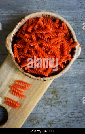 High-Angle Shot eine Steingut-Schüssel voller ungekochte rote Linsensuppe Fusilli auf einem grauen rustikalen Holztisch Stockfoto