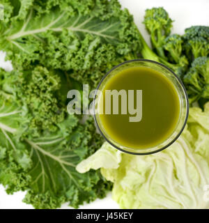 High-Angle Shot eine Grünkohl-Smoothie serviert in einem Glas und einige Blätter von Kale auf weißem Hintergrund Stockfoto