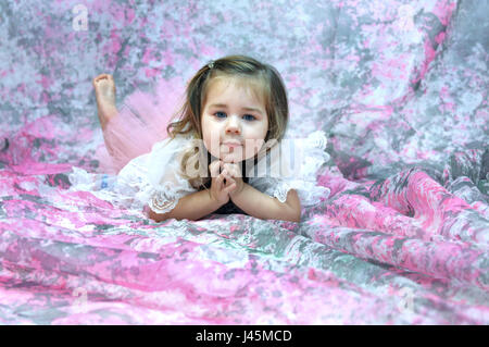 Baby Ballerina legt auf einem Boden von rosa und grau.  Sie ist barfuß, und sie lehnt ihren Kopf an ihren Händen.  Ihr Gesichtsausdruck ist nachdenklich. Stockfoto