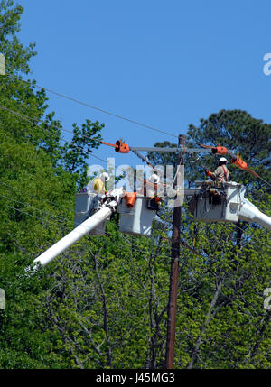 Drei Linemen führen Maintenace auf einen Strommast.  Drei Eimer heben Sie sie an die Spitze des Mastes, wie sie Teile ersetzen und Probleme zu beheben. Stockfoto