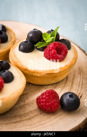 Leckere Törtchen mit Himbeeren und Heidelbeeren auf blauem Hintergrund Stockfoto