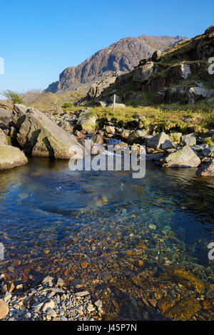 Kristallklare Wasser des Afon Nant Peris in Llanberis Pass mit den gewaltigen Klippen von Dinas Mot im Hintergrund mit Krippe Coch (Roter Kamm), ein kn Stockfoto