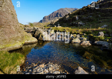 Kristallklare Wasser des Afon Nant Peris in Llanberis Pass mit den gewaltigen Klippen von Dinas Mot im Hintergrund mit Krippe Coch (Roter Kamm), ein kn Stockfoto