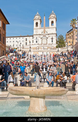 Spanische Treppe in Rom mit Touristen an einem sonnigen Tag mit blauem Himmel Trinità dei Monti Kirche im Hintergrund und Brunnen des hässlichen Boot Vordergrunds. Stockfoto