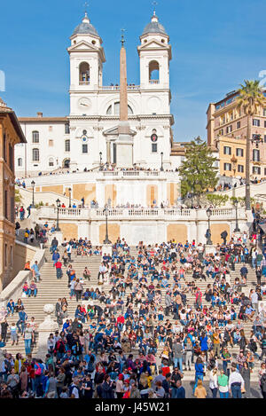 Spanische Treppe in Rom mit Massen von Touristen und Besucher an einem sonnigen Tag mit blauem Himmel und der Trinità dei Monti Kirche im Hintergrund. Stockfoto