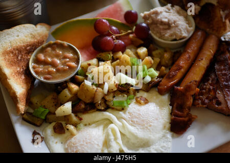 Komplettes Frühstück mit gebratenen Kartoffeln, Würstchen, Speck, Eiern, French-Toast, Grieben, Bohnen eine Früchte Stockfoto