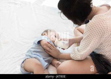 Asiatische Schwester füttert ihren kleinen Bruder und er trinkt Milch trinken aus der Flasche im Schlafzimmer zu Hause verwenden. Stockfoto