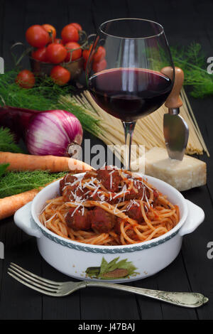 Schale mit Spaghetti und Fleischbällchen auf Tisch mit Glas Rotwein und frisches Gemüse. Stockfoto
