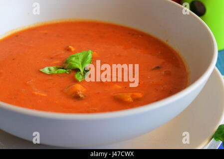 Tomatensuppe mit Muscheln in einer blauen Schüssel auf einem blauen Hintergrund mit Brot-sticks. Gesunde Ernährung-Konzept. Stockfoto