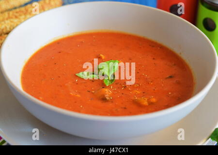 Tomatensuppe mit Muscheln in einer blauen Schüssel auf einem blauen Hintergrund mit Brot-sticks. Gesunde Ernährung-Konzept. Stockfoto