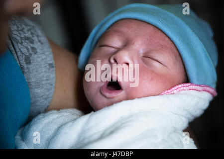 Foto ID: 534685885 ein neugeborenes Baby boy in weißen Decke und einem blauen knit Cap schläft in den Armen seiner Mutter mit offenem Mund und Augen gewickelt geschlossen Stockfoto