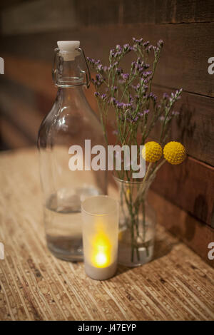 Gelb und Violett getrocknete Blumen und Lavendelblüten in Kugel Glas Glas zwischen Vintage Flasche Wasser und kleine Kerze auf Holz Tisch Stockfoto