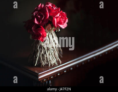 Bouquet von getrockneten roten Rosen mit verdrehten Stämmen in einem Bouquet in dunklen dramatische Beleuchtung auf einem polierten dunklem Hartholz Tisch Stockfoto