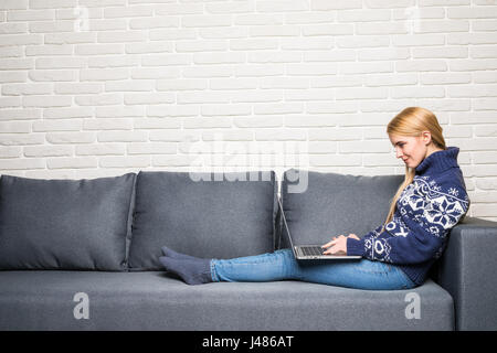 Nahaufnahme einer lächelnden Frau auf dem Sofa liegend mit Notebook im Wohnzimmer Stockfoto