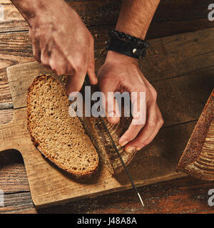 Clous Mann schneiden frisch gebackenes Brot auf einem alten Holzbrett flach zu legen Stockfoto