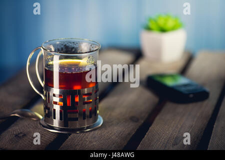 Das Glas mit Halter voller heißer, schwarzer Tee auf der Holzoberfläche Stockfoto