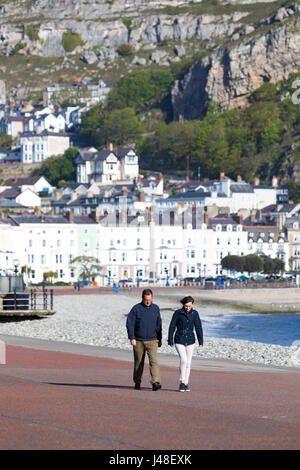 Eine männliche und weibliche paar zu Fuß entlang der Strandpromenade in Llandudno, rock Nordwales mit den Great Orme, Bildung und Hotels in der Ferne Stockfoto