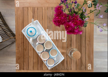 Teekanne und Tassen auf einem hölzernen Tavle mit einer Vase mit Blumen, von oben gesehen Stockfoto